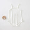 White lightweight cotton strappy romper for babies lying on a white surface with a wooden bear ring nearby