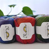 A collection of hand-dyed merino wool yarn spools in various colors, including purple, orange, pink, and green.