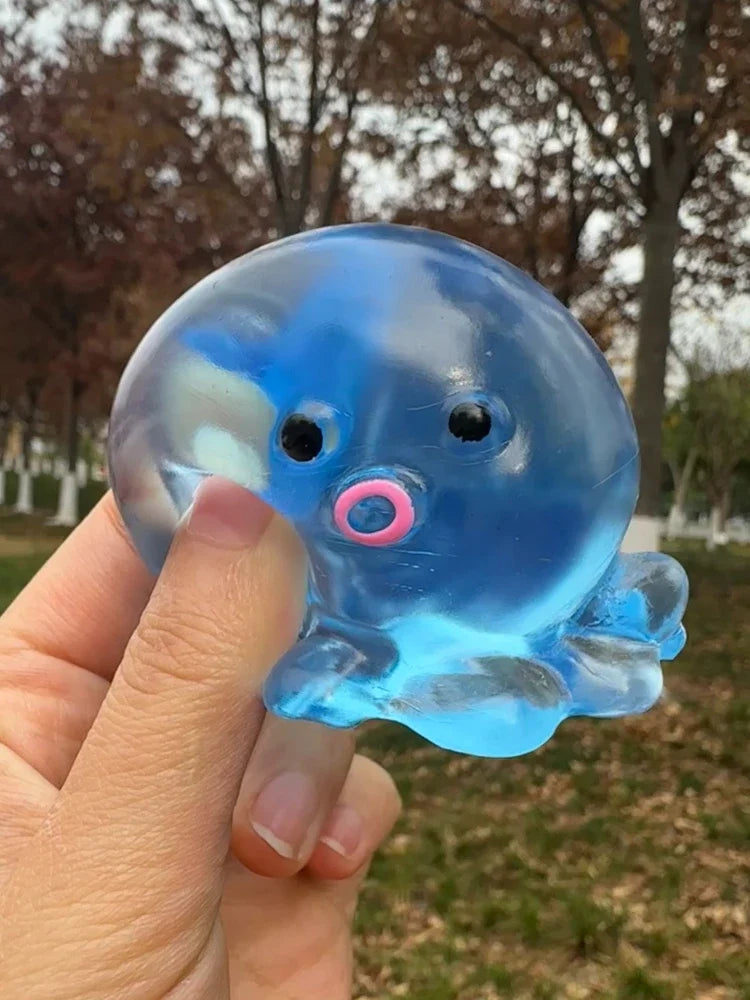 A hand holds a translucent blue squishy ocean octopus fidget toy with black eyes and a pink ring on its body.