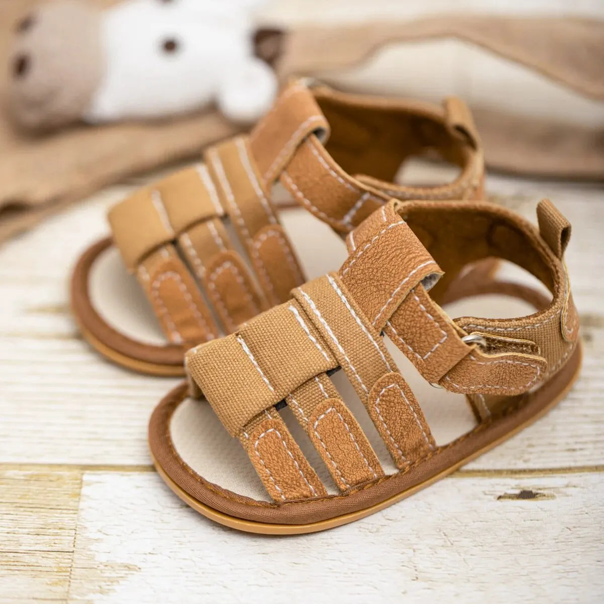 A pair of tan soft non-slip baby sandals for first walkers resting on a light wooden surface.