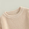 A close-up of a light pink knit pullover sweater with a ribbed neckline and textured body.