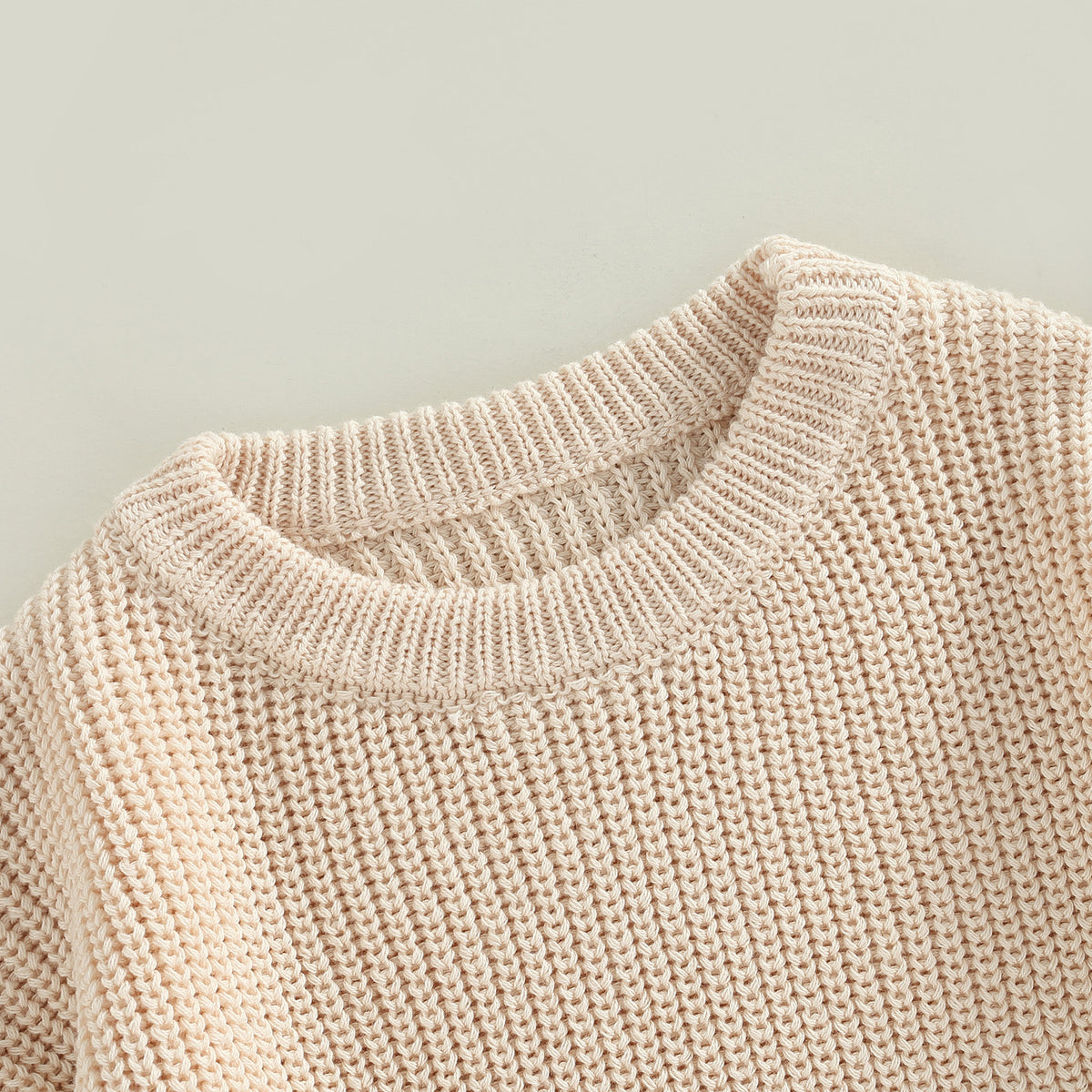 A close-up of a light pink knit pullover sweater with a ribbed neckline and textured body.