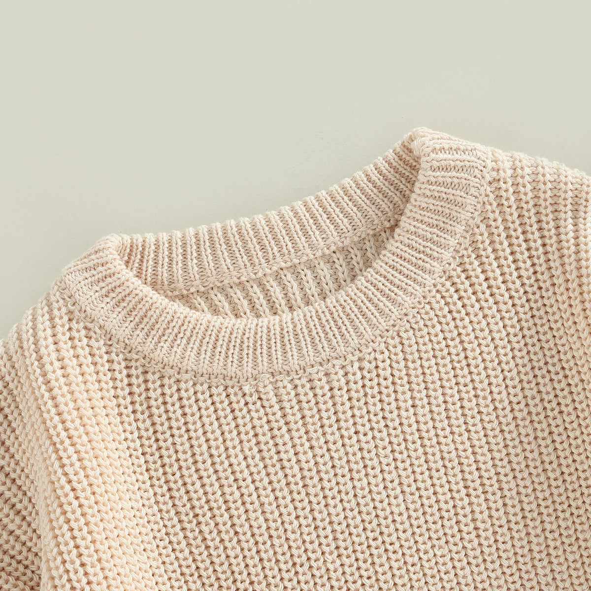 A close-up of a light beige knit pullover sweater with a ribbed neckline and textured body.