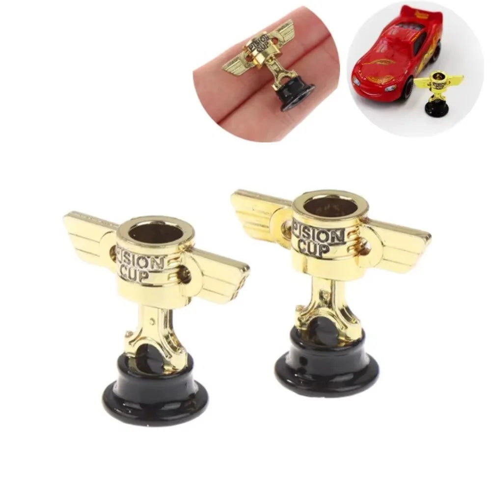 A miniature golden trophy cup with a black base and gold accents, shown next to a red car model.