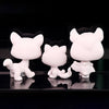 Three white bobble head figurines of cats in various poses displayed against a dark background.