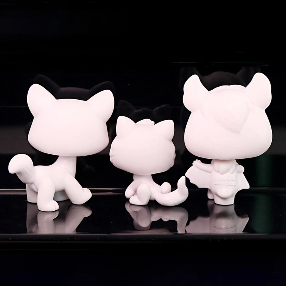Three white bobble head figurines of cats in various poses displayed against a dark background.