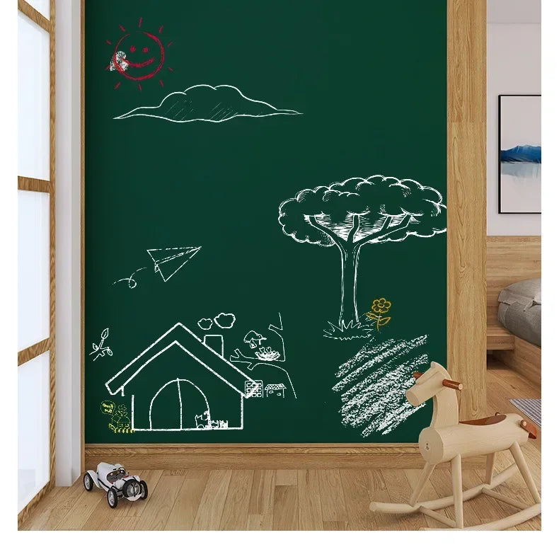 A green chalkboard wall sticker featuring hand-drawn white illustrations of a sun, clouds, trees, and a house.