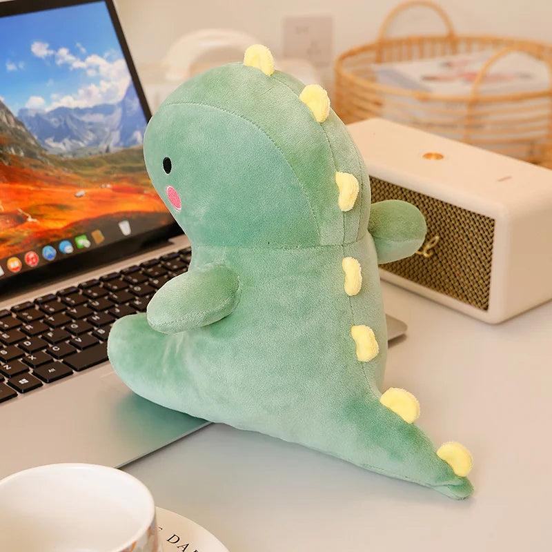 A soft, light green dinosaur plush toy with yellow spikes resting on a white desk next to a laptop.
