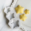A white silicone mold set featuring star-shaped cavities for baking and crafts, with yellow silicone stars displayed nearby.