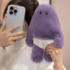 A person is holding a purple monster plush doll with white pants and a white sweater.