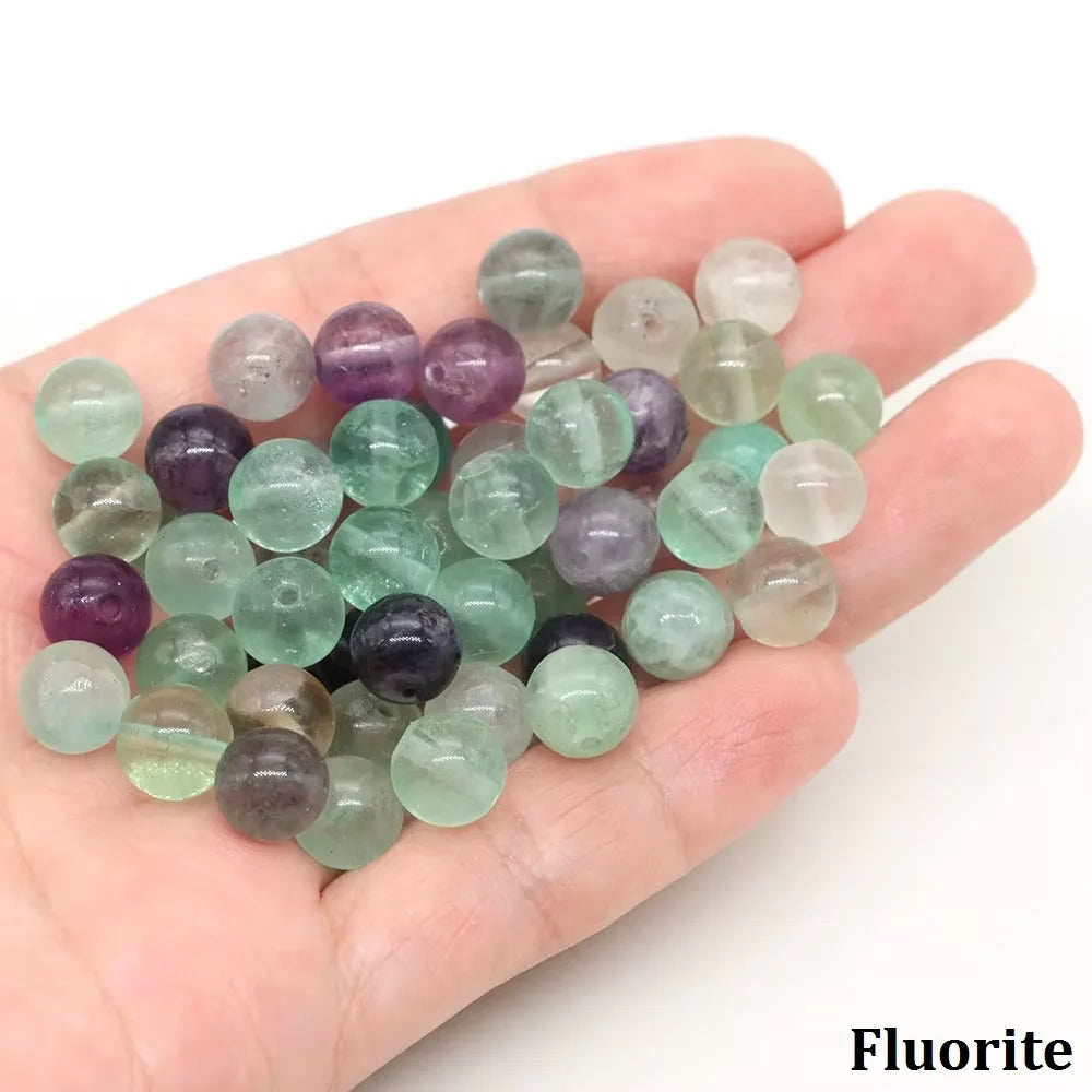A handful of round fluorite beads in shades of green, purple, and clear are held in a hand.