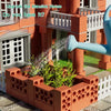A miniature brick building set featuring an orange house with white trim and a blue garden hose.