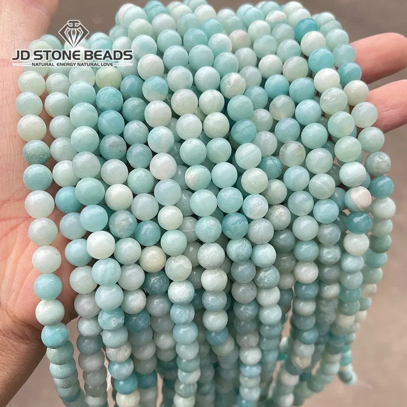 A hand holds a thick strand of light blue and white natural Amazonite beads for jewelry making