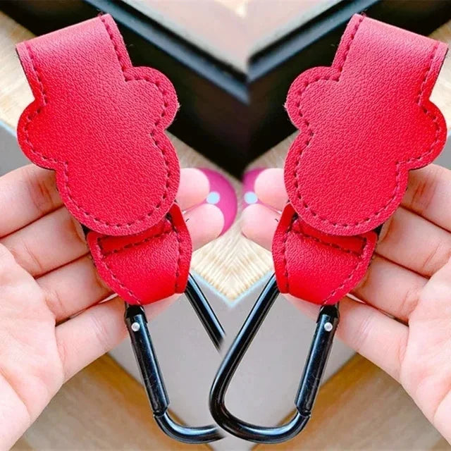A pair of red PU leather stroller organizer hooks with black clasps are shown being held in a hand.