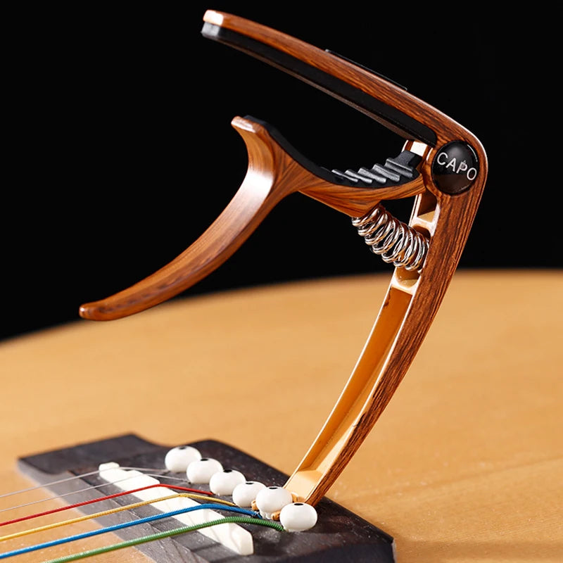 A wooden professional metal guitar capo with a pick holder resting on a guitar fretboard.