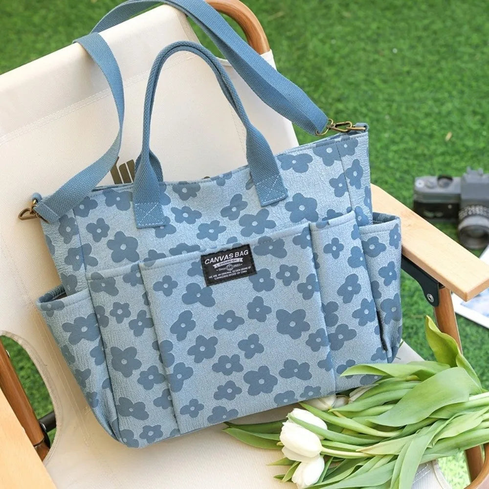 A light blue floral canvas tote bag with multiple exterior pockets resting on a wooden surface.