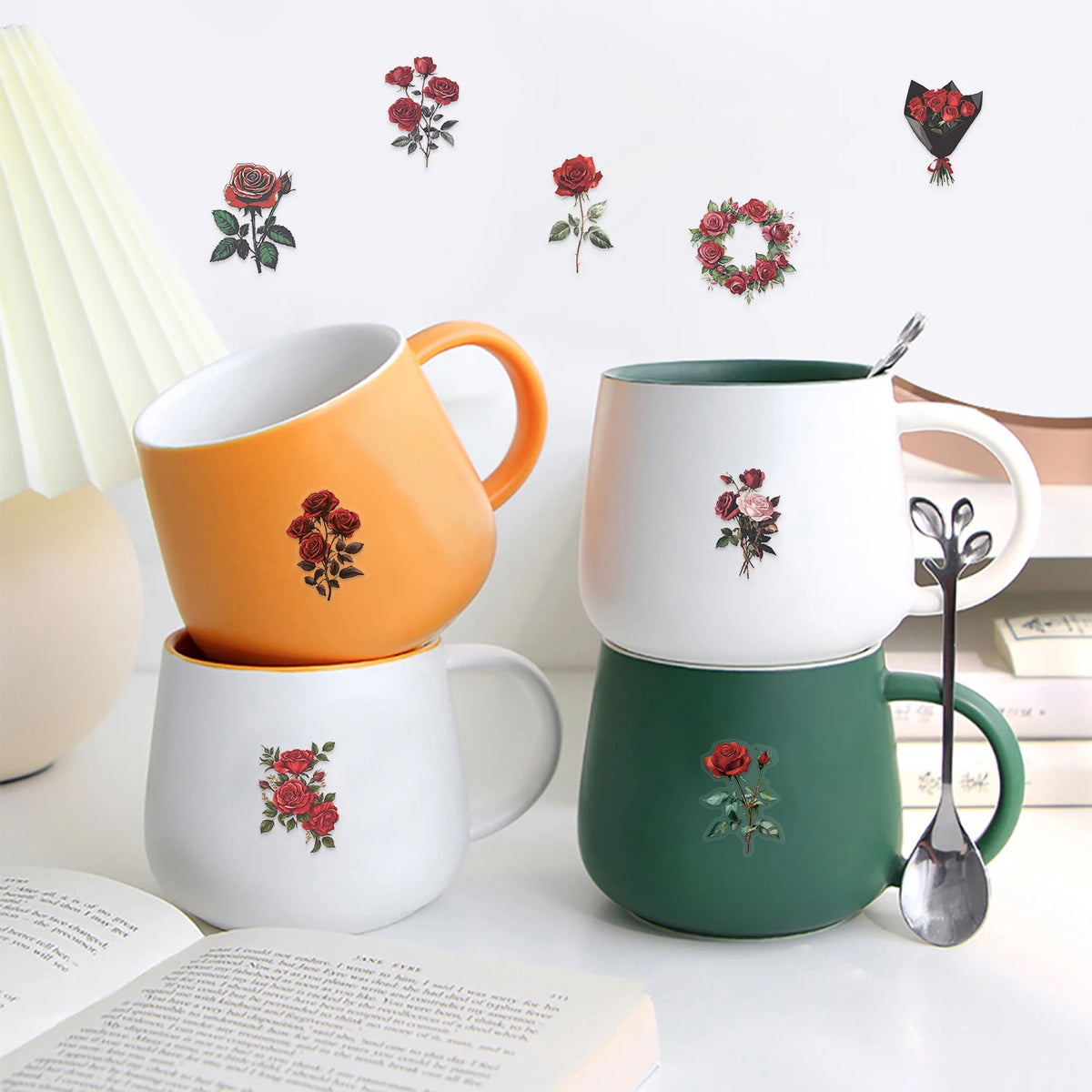 A set of ceramic mugs in white and orange colors with red rose designs displayed on a white surface.