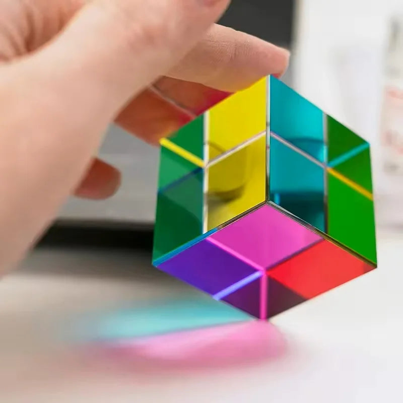 A hand holds a vibrant CMY prism cube, showing various color combinations and facets.