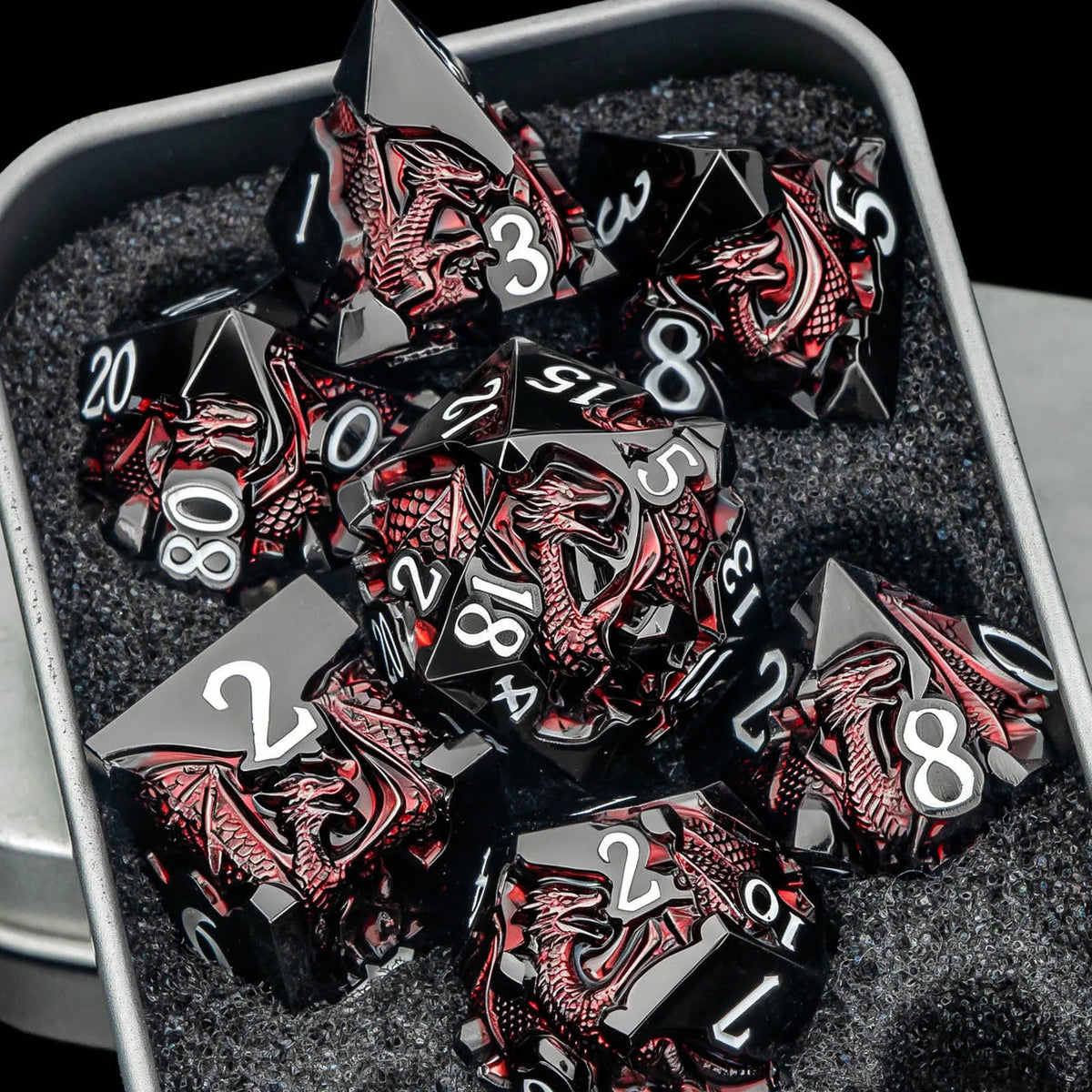 A set of black metal dice featuring a dragon design are displayed in a dark gray container.