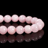 A line of natural pink quartz stretch bracelets lying on a reflective black surface.