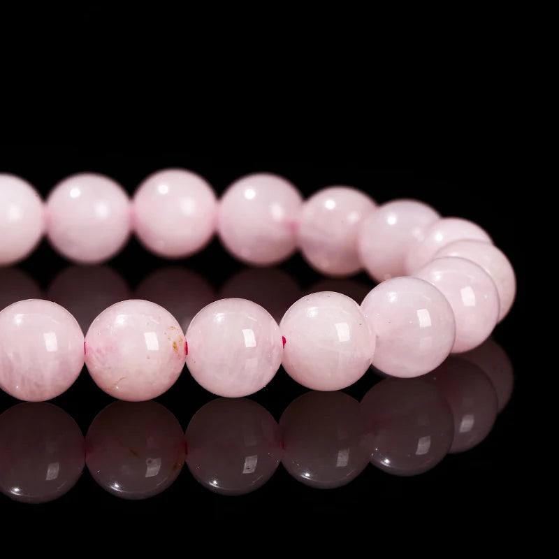 A line of natural pink quartz stretch bracelets lying on a reflective black surface.