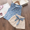 A set of floral blue patterned chiffon sleeveless top and beige shorts for girls displayed on a wooden surface.