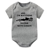 A gray knitted baby romper features text that reads I'm watching racing with daddy