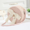 A light pink handwoven straw crossbody bag featuring a delicate white lace bow and strap.
