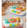 A pink musical baby piano playmat with a light-up keyboard and hanging toys is shown on a table.