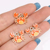 A set of orange and yellow enamel marine life charms shaped like crabs and lobsters displayed on a hand.