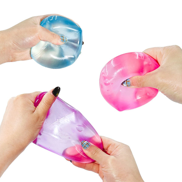Hands hold two translucent silicone fidget cubes, one blue and one pink, demonstrating the product for stress relief.