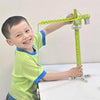 A young boy is operating a green diecast construction crane model toy set on a white table.