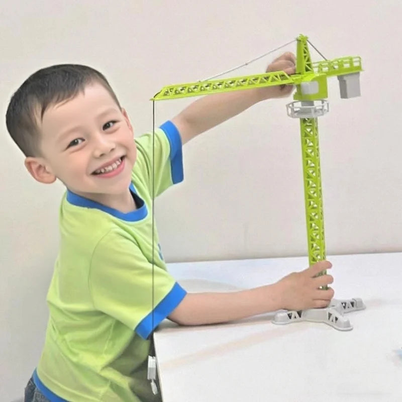 A young boy is operating a green diecast construction crane model toy set on a white table.