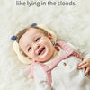 A smiling baby wearing a soft silicone head protection pillow while lying on fluffy white fur.