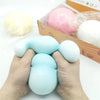 A hand is squeezing a light blue giant squishy stress ball next to a pink one and a white one in their box.