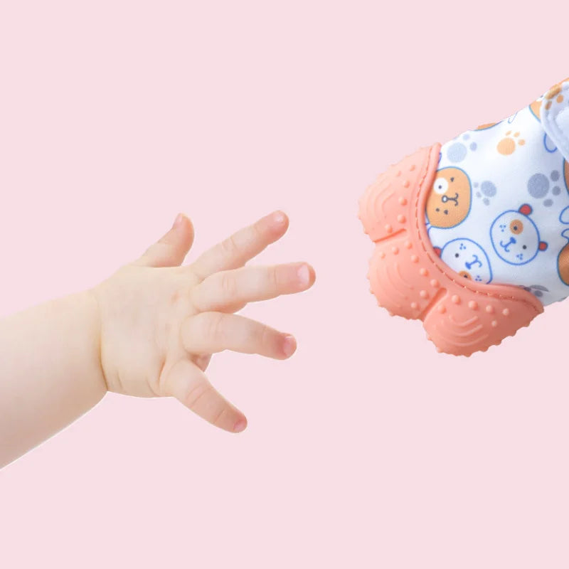 A hand is shown interacting with a soft, pink silicone teething mitten featuring a cartoon bear design.