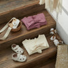 A pink knit ruffle romper and matching headband displayed on a wooden step.
