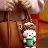A brown leather handbag held by a person wearing a pink sweater, featuring a Miffy bakery plush keychain charm.