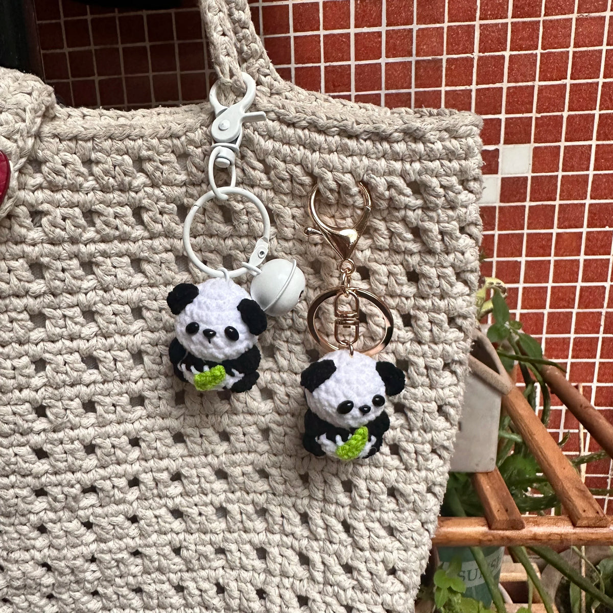 A beige crochet tote bag with a white and black panda charm keyring hanging from the strap.
