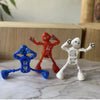Three wind-up dancing robot toys in red, blue, and white standing on a marble surface.