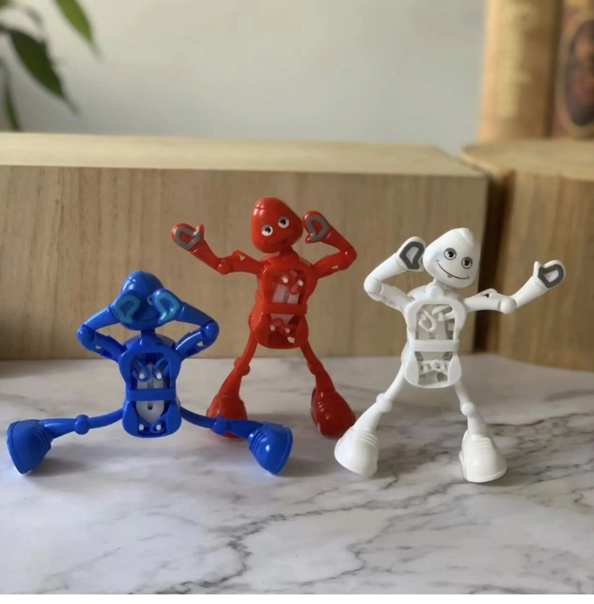 Three wind-up dancing robot toys in red, blue, and white standing on a marble surface.