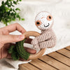 A hand holds an otter wooden baby rattle and teether ring with a green fabric attached on a light background.
