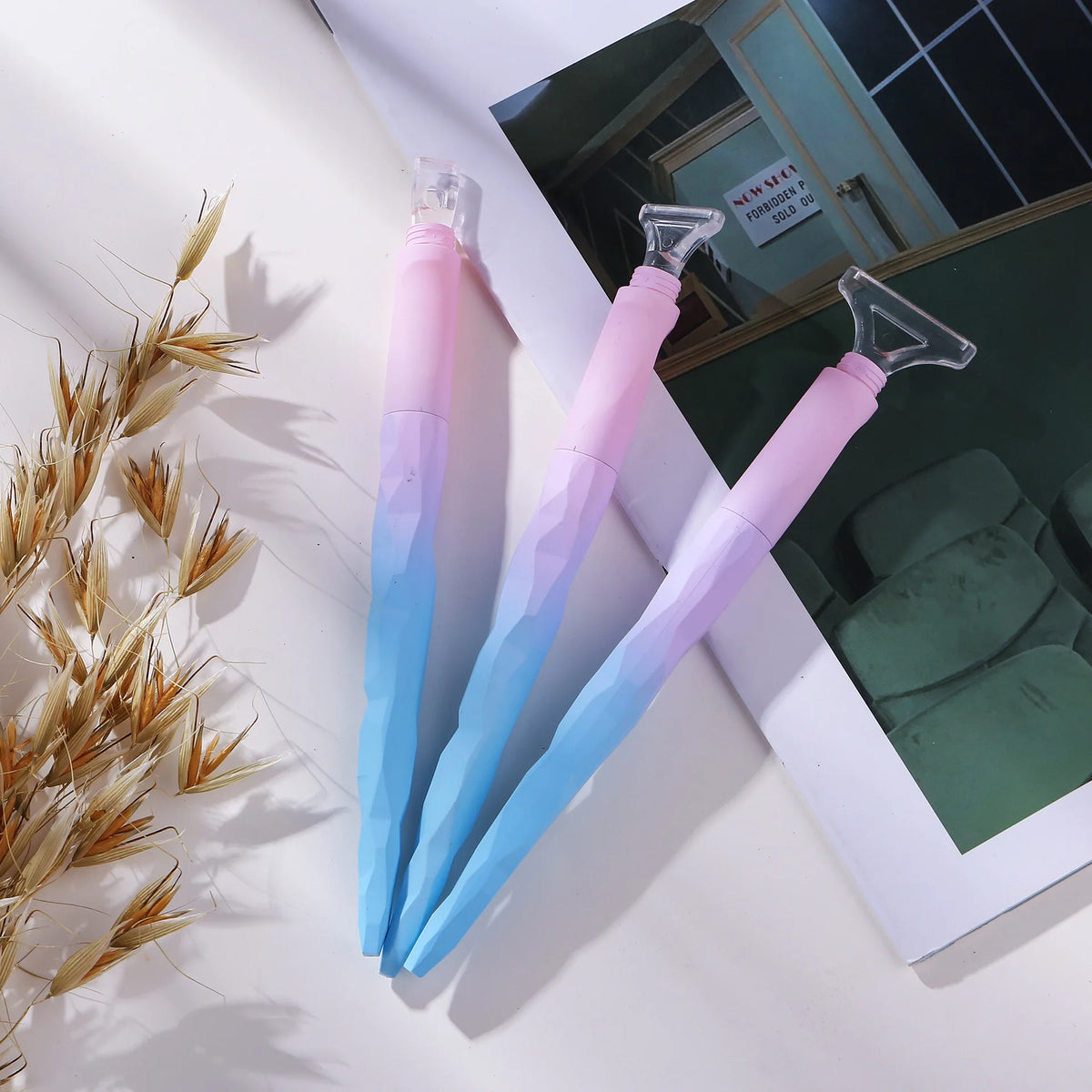A set of pink and blue diamond painting pens with roller tools displayed on a white surface next to a green background.
