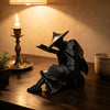 A dark, 3D printed samurai warrior figurine with a sword is displayed on a wooden surface next to a lit candle.