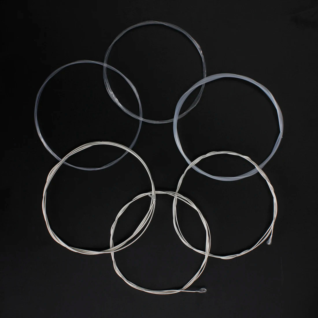 A collection of six silver-plated classical guitar strings with transparent nylon cores arranged in a star pattern.