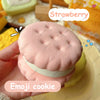 A pink strawberry flavored emoji cookie is shown resting on a yellow surface.