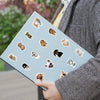 A hand holds a laptop featuring various funny dog stickers on a light blue background.