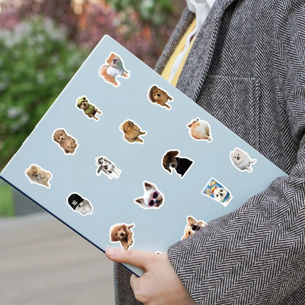 A hand holds a laptop featuring various funny dog stickers on a light blue background.