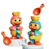 Un jouet de bain en forme de canard jaune avec une cuillère orange et une figurine de canard vert sur un support blanc.
