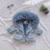 A light blue denim jacket with a fluffy blue faux fur collar lying on a white sheet.